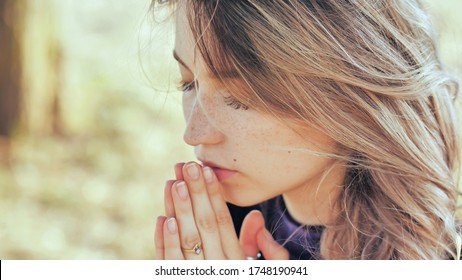 A young blonde 18 year old girl prays with folded hands.