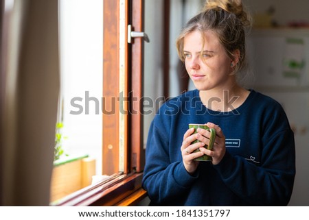 Young blonde blue-eyed girl drinking tea looking out the window