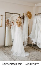 Young blonde bride trying on wedding dress in a showroom, looking in the mirror.