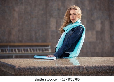 Young Blonde Business Woman With Long Curly Hairs Leaning On Parapet Stylish Fashion Model In Denim Jacket And Light Blue Scarf