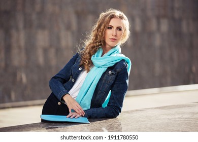 Young Blonde Business Woman With Long Curly Hairs Leaning On Parapet Stylish Fashion Model In Denim Jacket And Light Blue Scarf