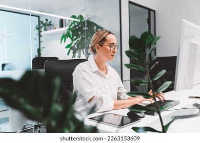 Young blonde business woman working on computer in her office, green plant blocking some of the view - Powered by Shutterstock