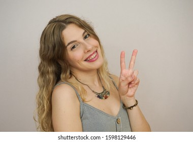 Young Blonde Caucasian Lady With Braces Or Brackets Is Looking At The Camera And Smiling At Neutral Grey Background. Her Orthodontic Treatment Is Ceramic Braces.