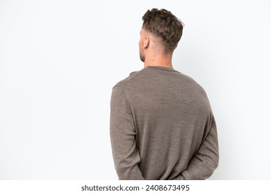 Young blonde caucasian man isolated on white background in back position and looking back