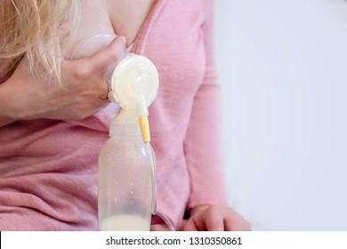 Young blonde caucasian mother in pink sweater is using single electric breast milk pump to pump breast milk for her baby. Copy space. Breast pumping human milk. space.