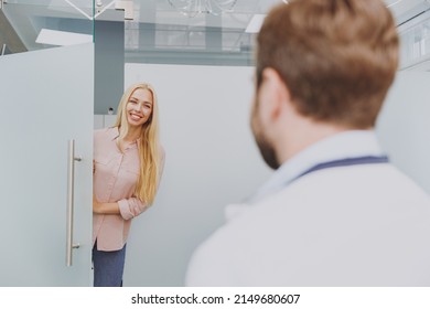 Young Blonde Caucasian Satisfied Happy Calm Calm Fun Woman 20s Enter Dental Office Indoor Light Modern Cabinet Greeting Male European Doctor Stomatologist Healthcare Oral Enamel Aesthetic Treatment.