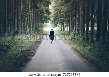 young blonde caucasian woman walking on narrow road through dark forest