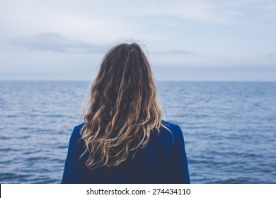 young blonde curly girl looking at hazy sunshine through a thick mist on a calm sea and blue skies back view