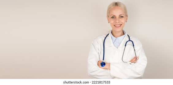 Young blonde doctor standing against gray background smiling at camera.Copy space banner.Place for text - Shutterstock ID 2221817533