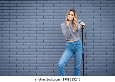 Young Blonde Female Comedian Against Blue Grey Brick Wall With Microphone And Expressions 