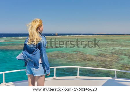 Young blonde female on yacht looking at turquoise coral reefs in Red Sea