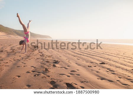 A young blonde female tourist does a cartwheel on the sand at Tafedna Beach in the province of Essouira, Morocco.