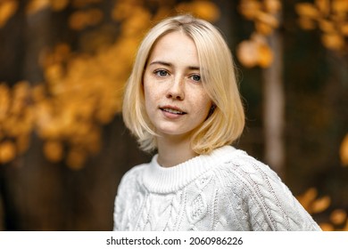 young blonde with freckles short haircut white sweater in autumn in the park
