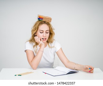 Young blonde girl balancing books on her head at a table, usure weather she will pass her classes, studying blonde 