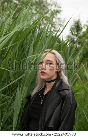 A young blonde girl in a black leather coat walks in the park and listens to music