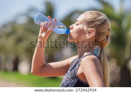 Young blonde girl drinking water during morning jogging