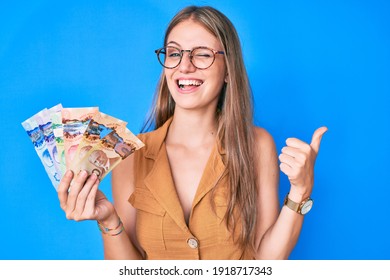 Young blonde girl holding canadian dollars winking looking at the camera with sexy expression, cheerful and happy face. 