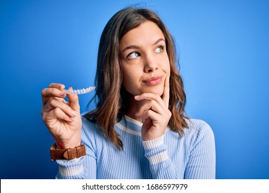 Young Blonde Girl Holding Dental Orthodontic Clear Aligner Over Blue Isolated Background Serious Face Thinking About Question, Very Confused Idea