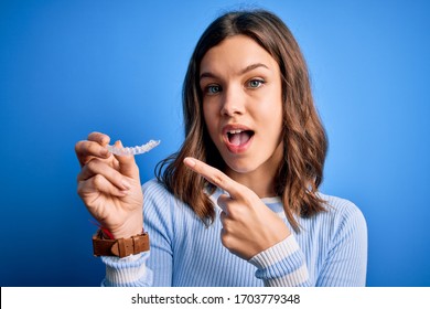 Young Blonde Girl Holding Dental Orthodontic Clear Aligner Over Blue Isolated Background Very Happy Pointing With Hand And Finger