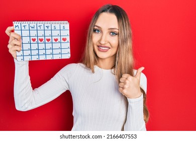 Young Blonde Girl Holding Heart Calendar Smiling Happy And Positive, Thumb Up Doing Excellent And Approval Sign 