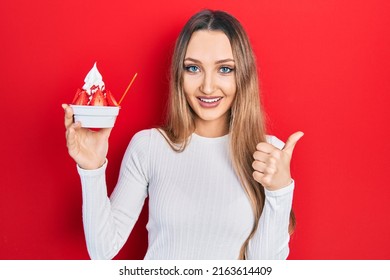 Young Blonde Girl Holding Ice Cream Smiling Happy And Positive, Thumb Up Doing Excellent And Approval Sign 