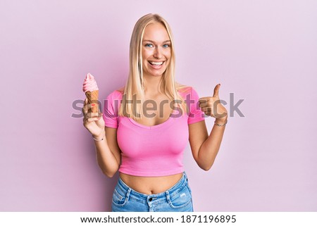 Young blonde girl holding ice cream smiling happy and positive, thumb up doing excellent and approval sign 