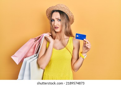 Young Blonde Girl Holding Shopping Bags And Credit Card Clueless And Confused Expression. Doubt Concept. 