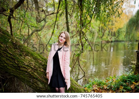 Young blonde girl at pink coat posed on autumn park.