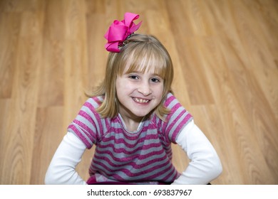 Young Blonde Girl Sitting On The Floor With Hot Pink Bow In Her Hair