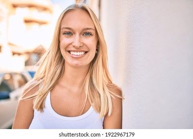 Young blonde girl smiling happy leaning on the wall at the city.