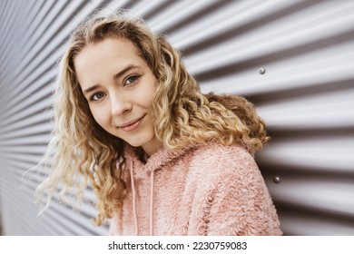 Young blonde girl standing in front of metal wall looking at camera smiling