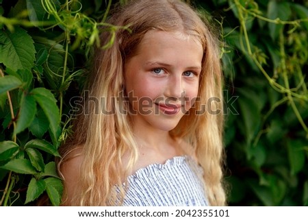 a young blonde girl stands in the leaves of wild grapes. High quality photo