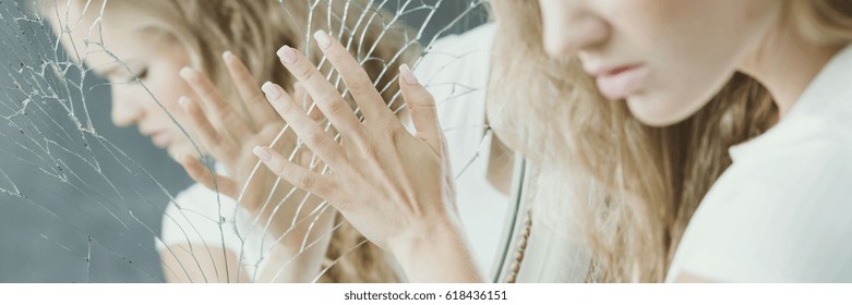 Young blonde girl touching the broken mirror