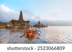 Young blonde girl in traditional red dress in the boat near Pura Ulun Danu Bratan temple - Hindu temple on Bratan lake - Bali island, Indonesia