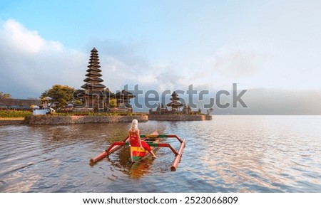Young blonde girl in traditional red dress in the boat near Pura Ulun Danu Bratan temple - Hindu temple on Bratan lake - Bali island, Indonesia
