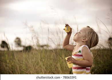 Young blonde girl trying to blow bubbles in a field graded with a vintage tone
