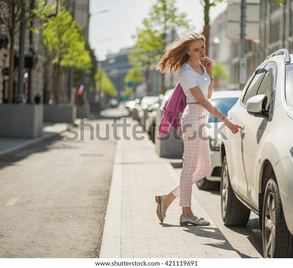 young blonde girl walks through the streets of the\
city. center of Moscow. Summer hot sunny day. girl dressed in pink\
pants and white topic. girl stands near the car trying to open the\
door