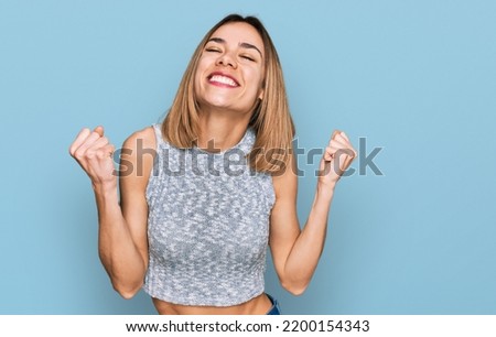 Young blonde girl wearing casual style with sleeveless shirt very happy and excited doing winner gesture with arms raised, smiling and screaming for success. celebration concept. 