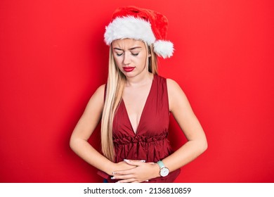 Young Blonde Girl Wearing Christmas Hat With Hand On Stomach Because Indigestion, Painful Illness Feeling Unwell. Ache Concept. 