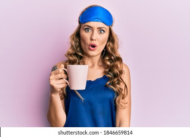 Young Blonde Girl Wearing Sleep Mask And Pyjama Drinking Coffee Scared And Amazed With Open Mouth For Surprise, Disbelief Face 