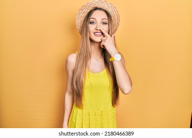 Young Blonde Girl Wearing Summer Hat Pointing With Hand Finger To Face And Nose, Smiling Cheerful. Beauty Concept 