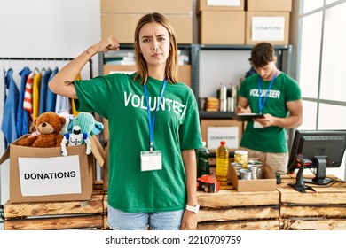 Young Blonde Girl Wearing Volunteer T Shirt At Donation Stand Strong Person Showing Arm Muscle, Confident And Proud Of Power 