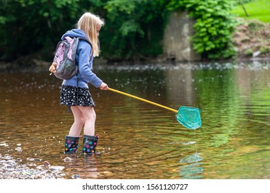 Young blonde girl wish fishing net wading into river - Powered by Shutterstock