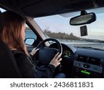 Young blonde long-haired girl driving the grand tourer car at sunset on a long trip.Interior view, good driver, attentive and with her hands on the wheel. Dusk with reddish sky