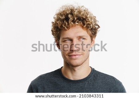Young blonde man with curly hair smiling and looking aside isolated over white wall