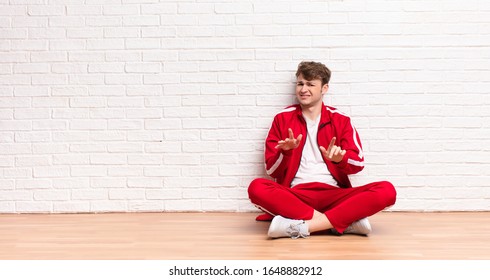 Young Blonde Man Feeling Disgusted And Nauseous, Backing Away From Something Nasty, Smelly Or Stinky, Saying Yuck Sitting On The Floor