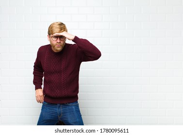 young blonde man looking bewildered   astonished  and hand over forehead looking far away  watching searching agaist vintage tiles wall