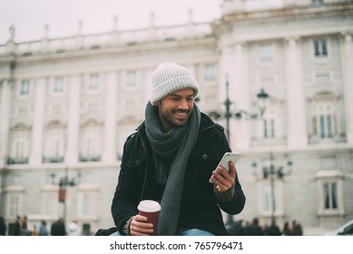 Young Blonde Man On The Mobile Phone And Drinking Coffee Near The Royal Palace In Winter  
