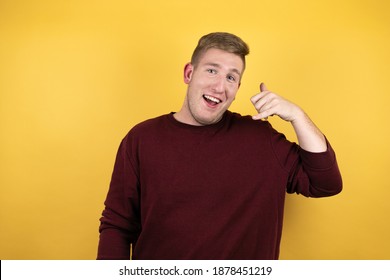 Young blonde man wearing a casual red sweater over yellow background smiling doing phone gesture with hand and fingers like talking on the telephone - Shutterstock ID 1878451219