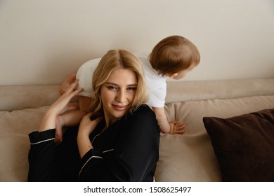 Young blonde mother having quality time with her baby boy son at family home flat - Wearing black budoir dress costume sleeping gown
